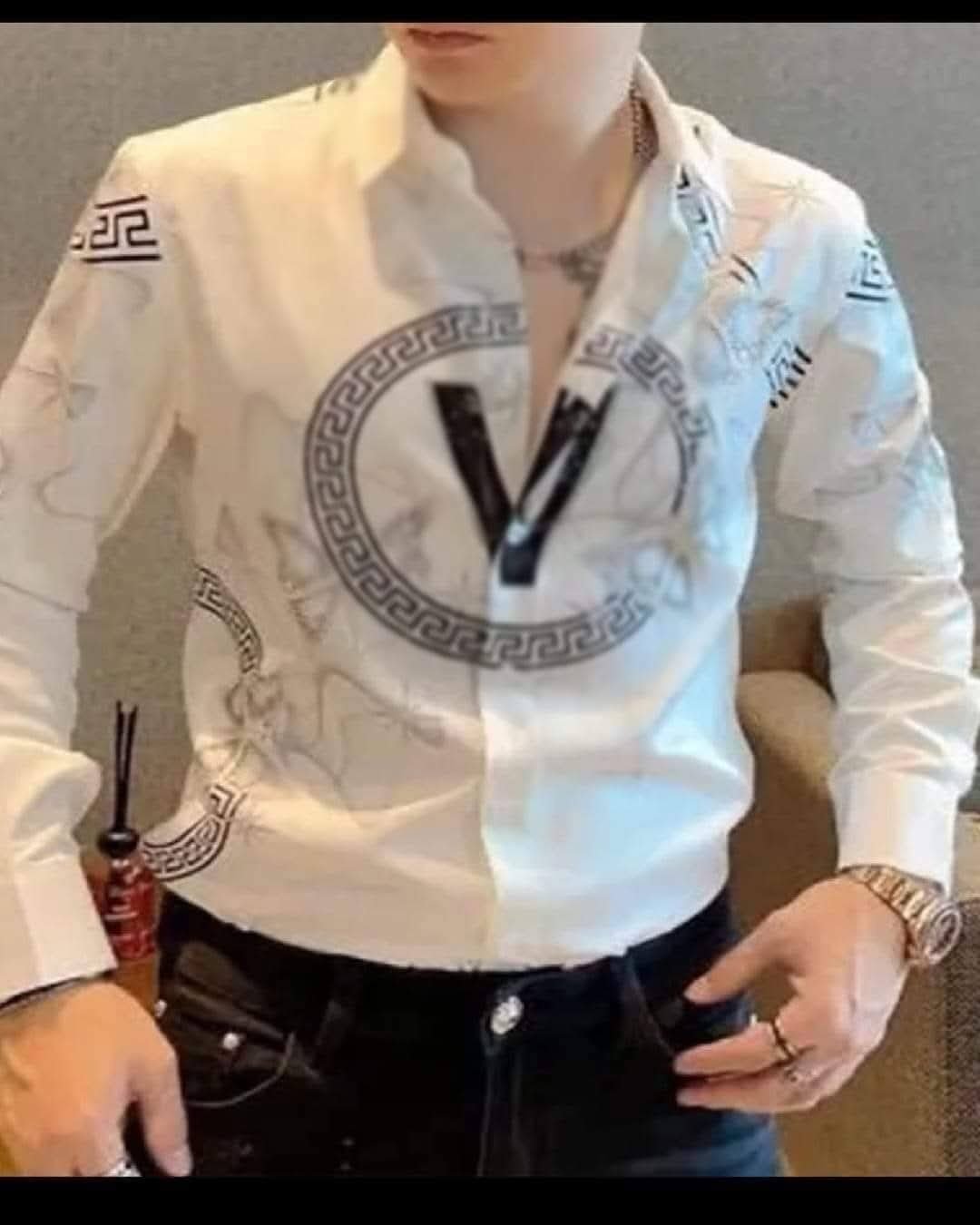 Cămașa este predominant albă, dar are imprimeuri mari, în principal în tonuri de gri și negru, pe partea din față și pe mâneci.